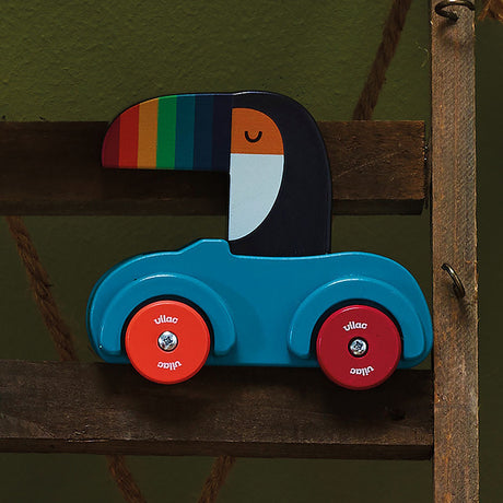 Vilac wooden toucan toy car with a rainbow beak, blue body, and red wheels, displayed on a wooden shelf.