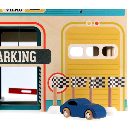 Blue wooden toy car in front of a Vilac wooden parking garage with racing flags and yellow garage door.