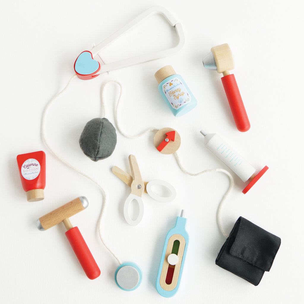 Toy medical kit with colorful wooden tools, including a stethoscope, syringe, scissors, and pill bottle, arranged on a white background. Playful tone.