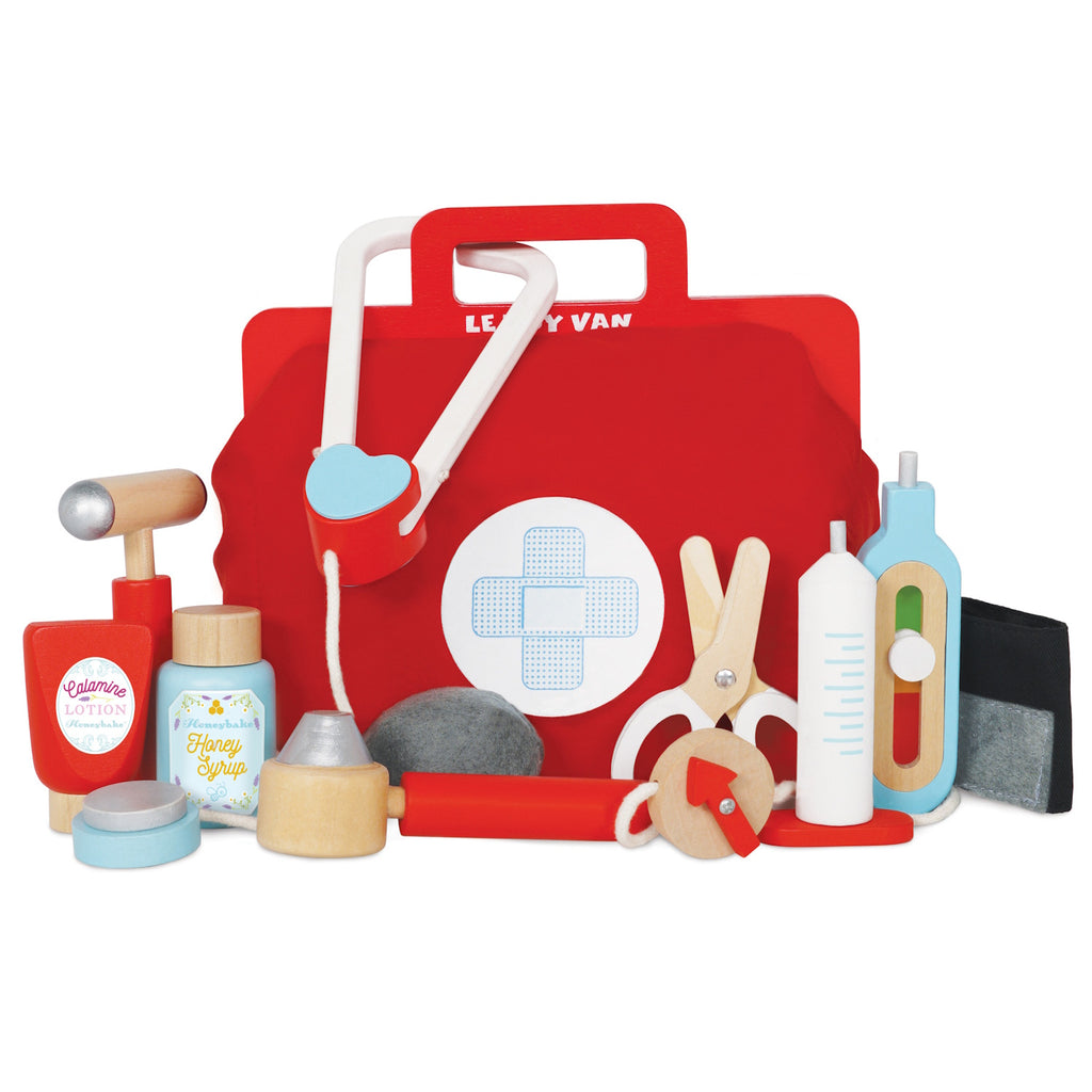 A vibrant red toy medical bag with a white cross symbol, surrounded by wooden toy instruments like a syringe, scissors, a stethoscope, and medicine bottles.