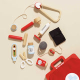 Flat lay of wooden doctor roleplay accessories scattered next to the top corner of the red medical bag.