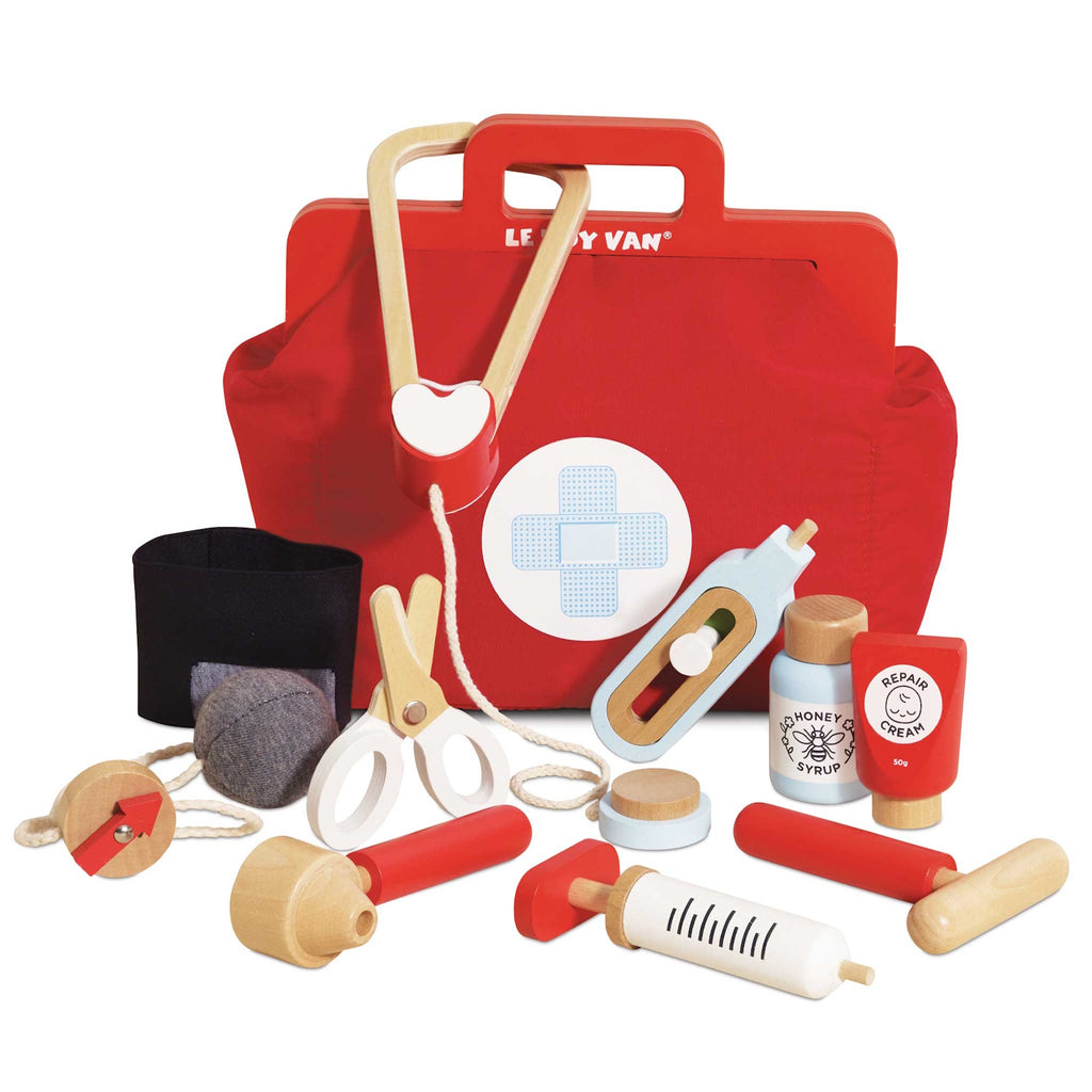A vibrant red toy medical bag with a white cross symbol, surrounded by wooden toy instruments like a syringe, scissors, a stethoscope, and medicine bottles.