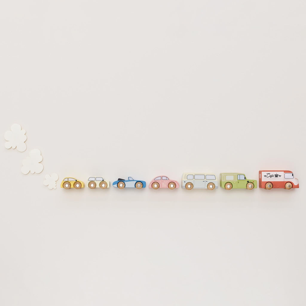 Colorful wooden toy vehicles on display include a red café truck, green SUV, blue sports car, yellow taxi, pink car, cream bus, and beige camper.