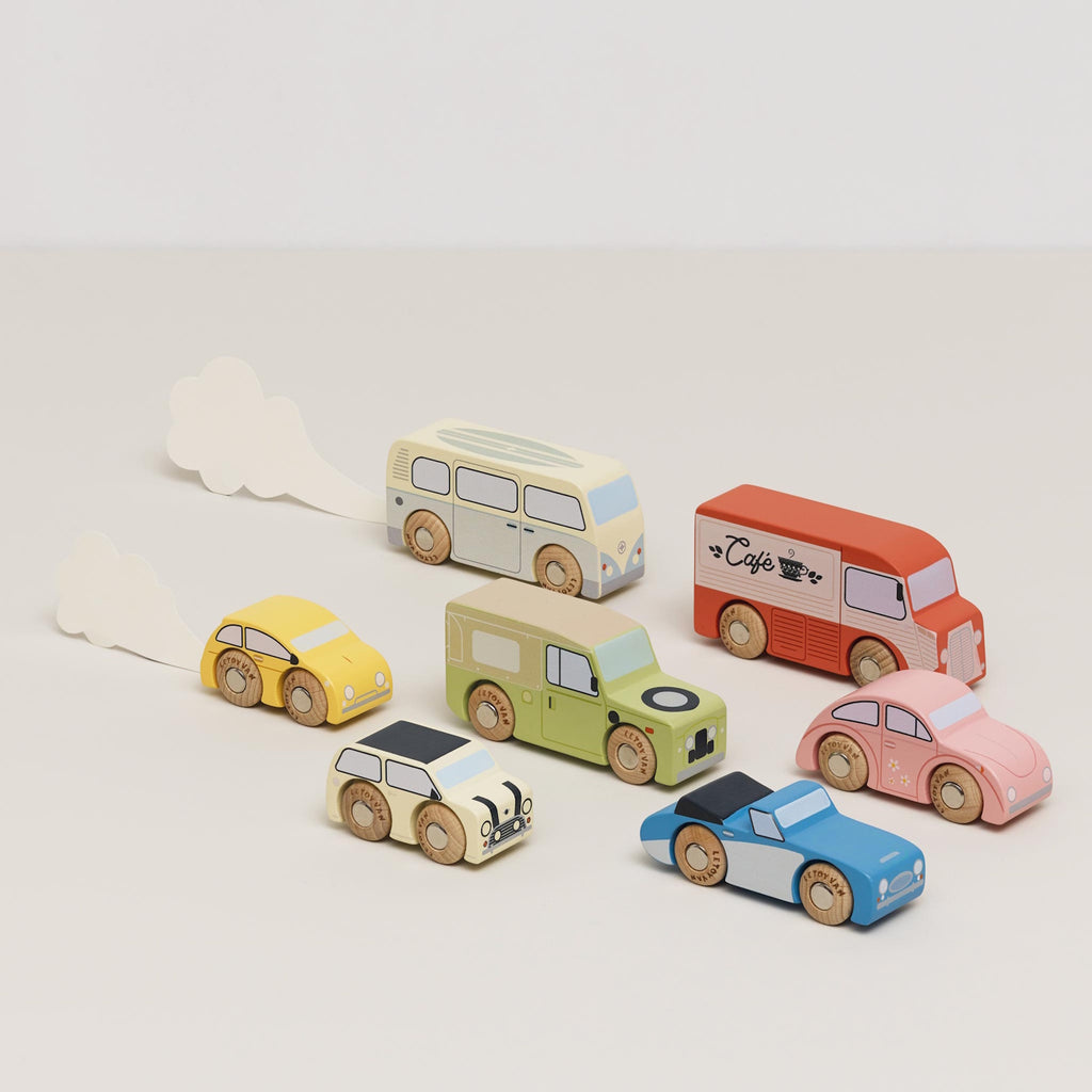 Colorful wooden toy vehicles on display include a red café truck, green SUV, blue sports car, yellow taxi, pink car, cream bus, and beige camper.