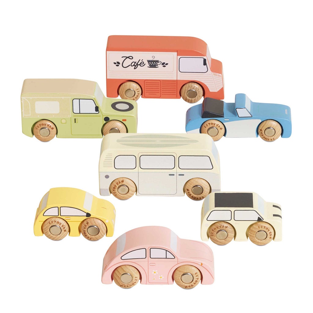 Colorful wooden toy vehicles on display include a red café truck, green SUV, blue sports car, yellow taxi, pink car, cream bus, and beige camper.