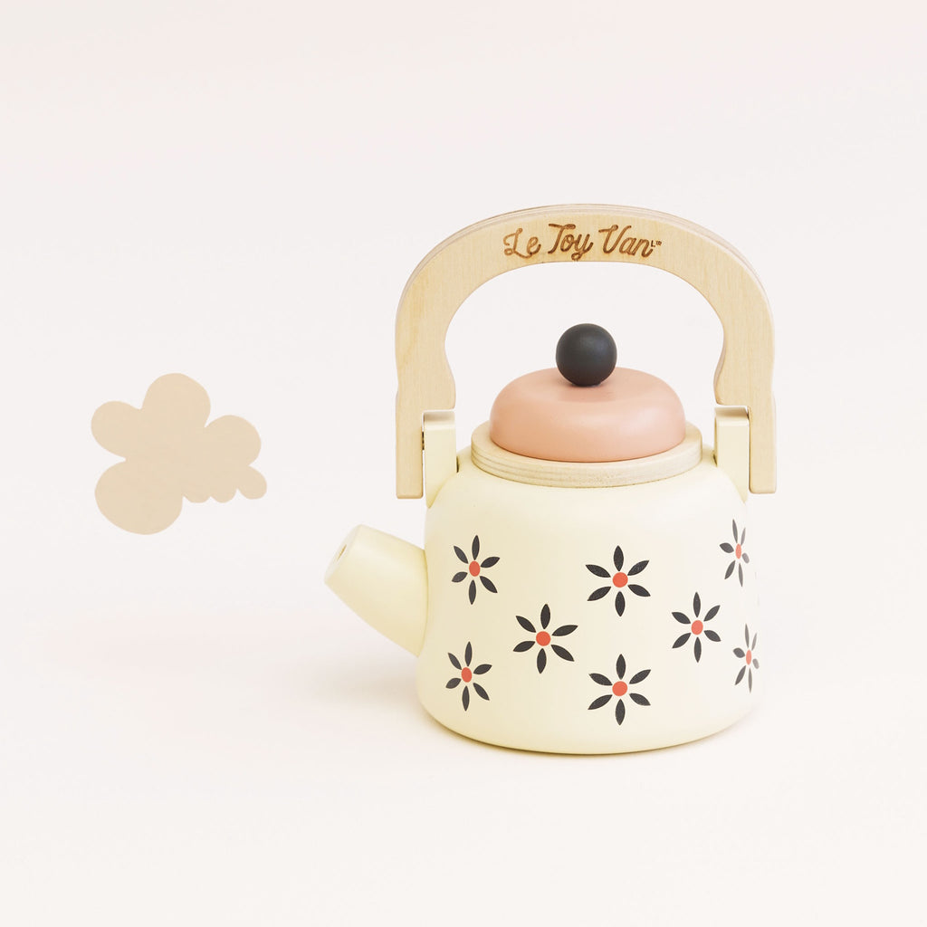 Toy teapot with a wooden handle and cream body, featuring black and orange floral patterns. The lid is peach-colored, creating a playful and nostalgic vibe.