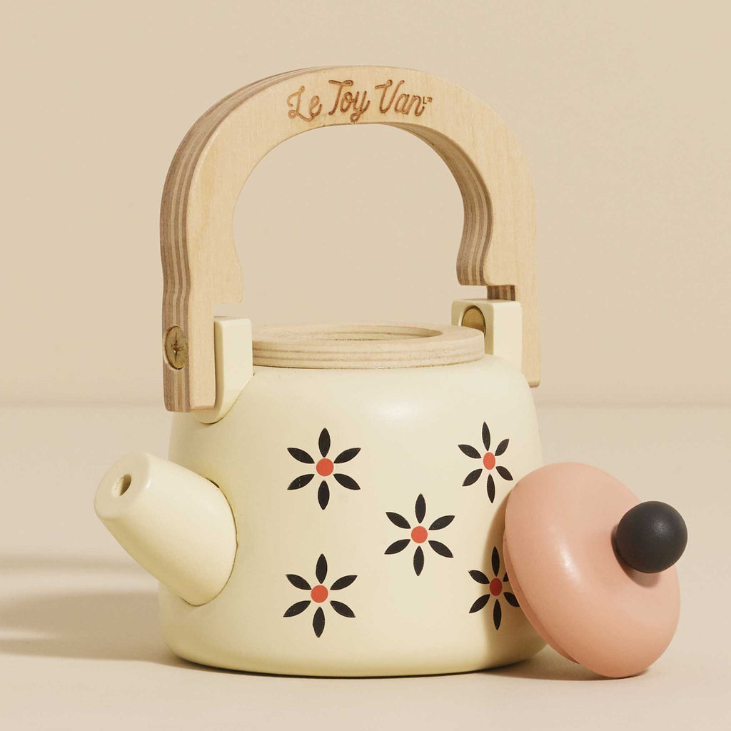 Toy teapot with a wooden handle and cream body, featuring black and orange floral patterns. The lid is peach-colored, creating a playful and nostalgic vibe.