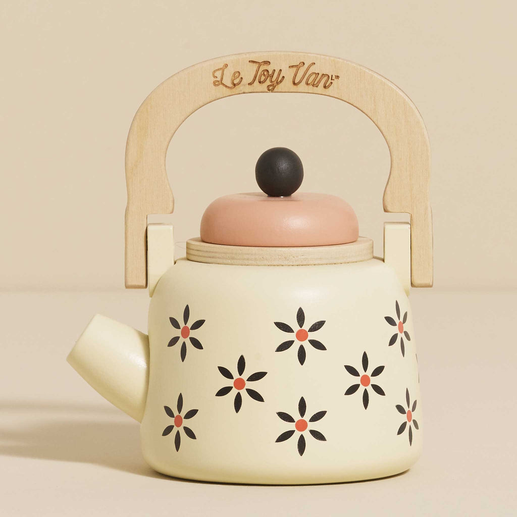 Toy teapot with a wooden handle and cream body, featuring black and orange floral patterns. The lid is peach-colored, creating a playful and nostalgic vibe.