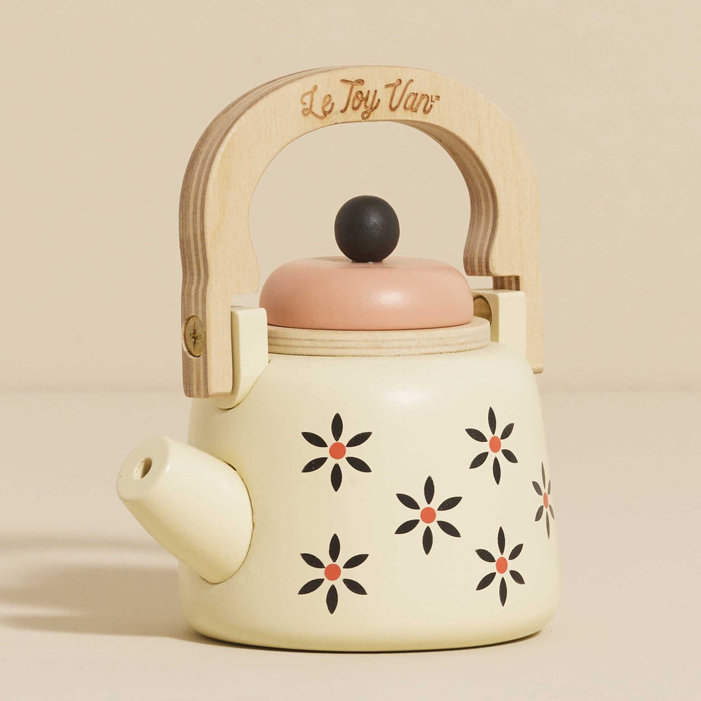 Toy teapot with a wooden handle and cream body, featuring black and orange floral patterns. The lid is peach-colored, creating a playful and nostalgic vibe.
