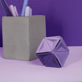 Purple silicone hexaflexagon fidget toy upright on a desk beside a concrete pen holder.