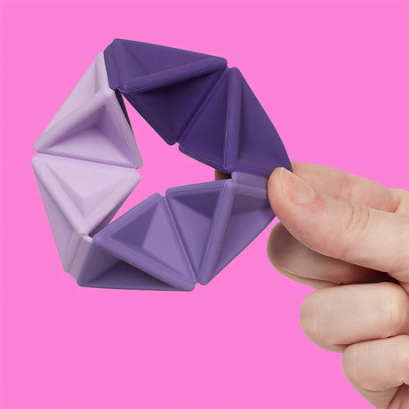 A hand flexing a purple silicone hexaflexagon fidget toy against a vibrant pink background.