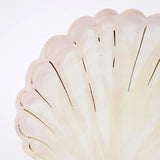A close-up of a seashell-shaped paper plate in pale pink and yellow with gold foil accents.