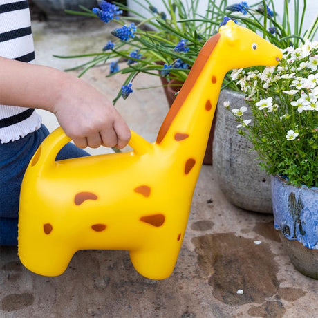 A yellow giraffe-shaped novelty watering can being used to water white flowers in a stone garden pot.