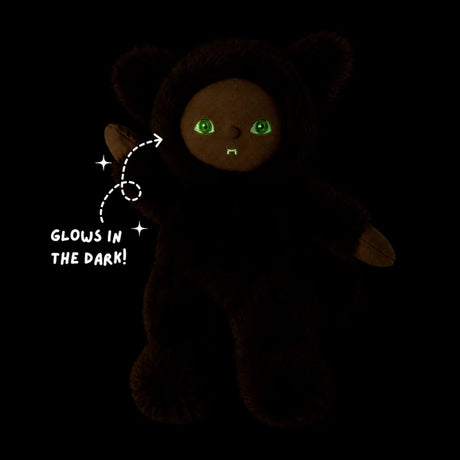 Werewolf plush doll glowing in the dark with bright green eyes and fangs against a black background.