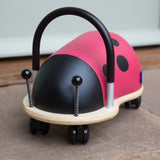 Small Wheely Bug ladybird ride on toy with a black handle, wooden base, and castor wheels on a patio.
