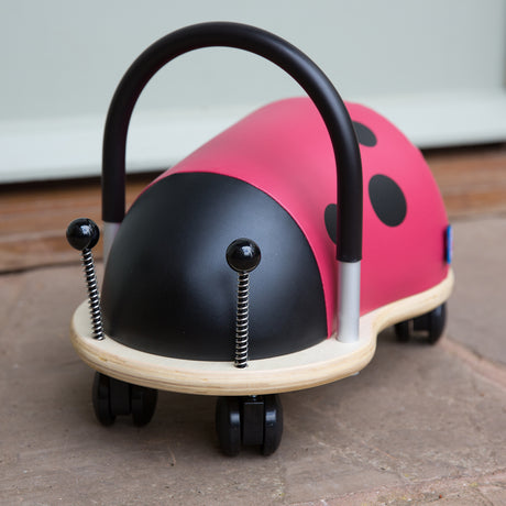 Small Wheely Bug ladybird ride on toy with a black handle, wooden base, and castor wheels on a patio.