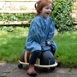 Happy toddler riding a Wheely Bug bumblebee ride on toy in a grassy garden.