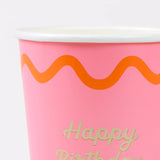 Close-up of a pink paper cup with an orange wavy line and gold text that reads "Happy Birthday".