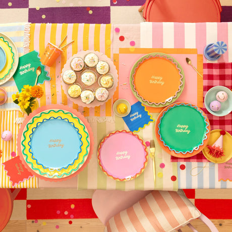 Colorful, top-down view of a birthday table setting with cupcakes, plates, napkins, and confetti.