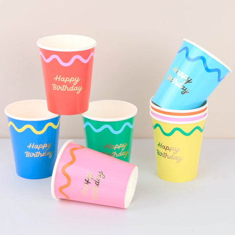 Colorful paper cups with wavy patterns and gold "Happy Birthday" text, stacked and arranged on a table.
