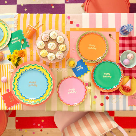 Overhead view of a colorful, patterned birthday table setting with vibrant paper plates and cupcakes.