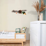 Plush flying mallard duck hanging above a wooden toddler bed in a neutral-toned, modern nursery.