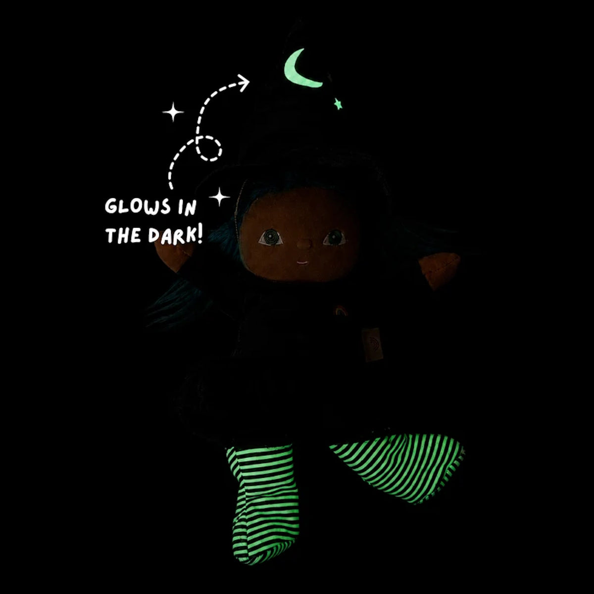 Plush witch doll in a dark room with green glow-in-the-dark moon on her hat and striped legs.