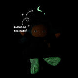Plush witch doll in a dark room with green glow-in-the-dark moon on her hat and striped legs.