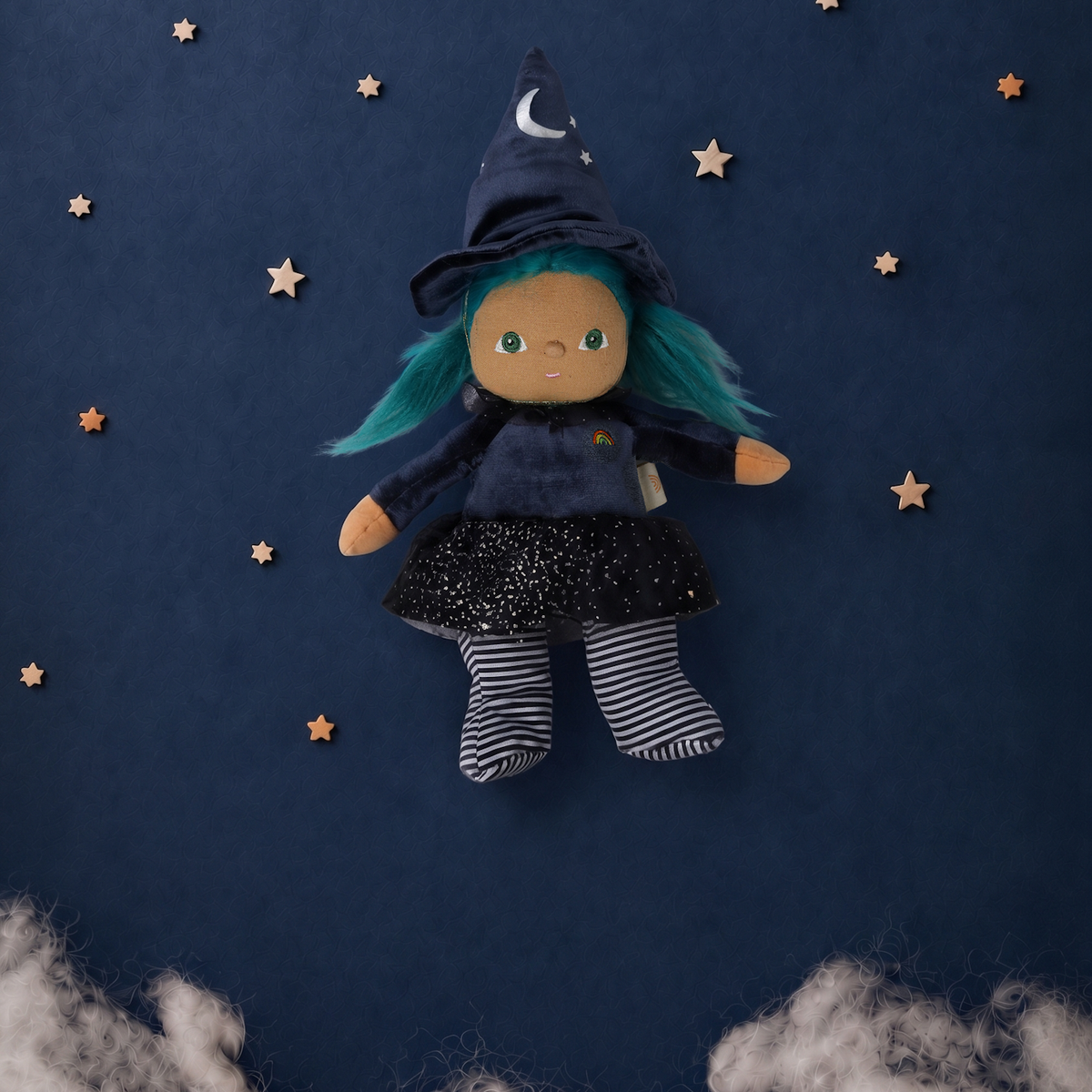 Plush witch doll with teal hair centered against a dark blue night sky backdrop with stars and clouds.