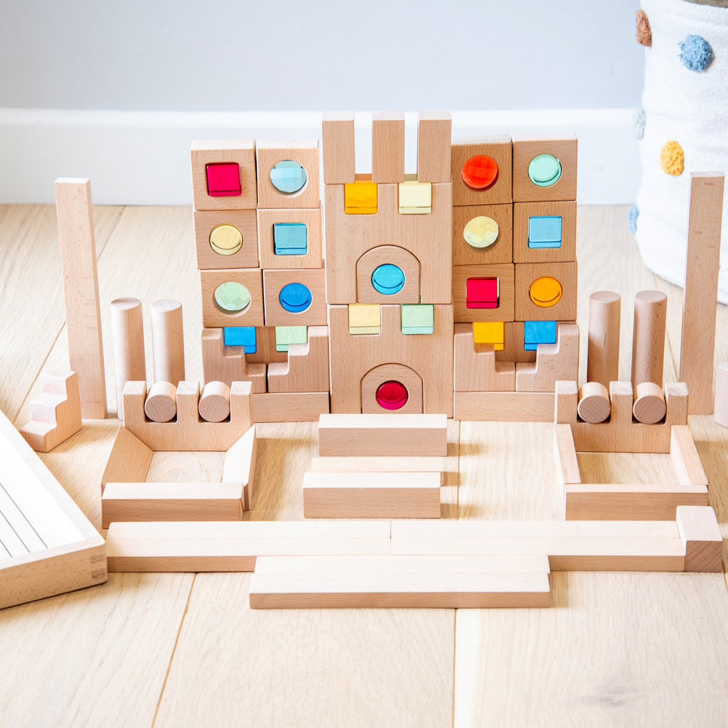 A large collection of wooden construction blocks with embedded colorful gems, designed to encourage creative building, light play, and sensory exploration.