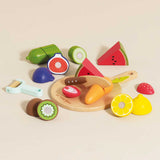 Wooden toy sliceable fruits and vegetables scattered around a chopping board on a beige surface.