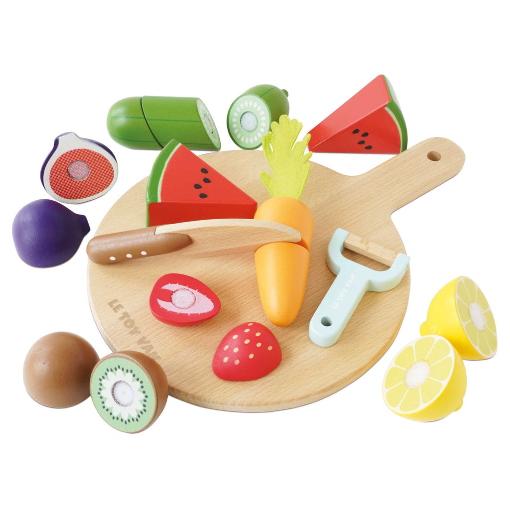 Wooden toy fruits and vegetables, including watermelon, kiwi, and carrot on a cutting board, with a toy knife and peeler, evoke playful cooking.