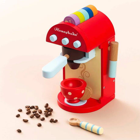 A wooden toy coffee machine by Honeybake surrounded by scattered coffee beans, a red cup, and a spoon.