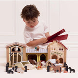 Child playing with a wooden farmyard stable playset, lifting the removable roof panels.