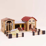Wooden farmyard toy stable set with red and stone-style buildings, fences, and two toy horses inside.