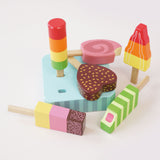 Six wooden toy ice lollies scattered around and on their light-blue base on a white surface.