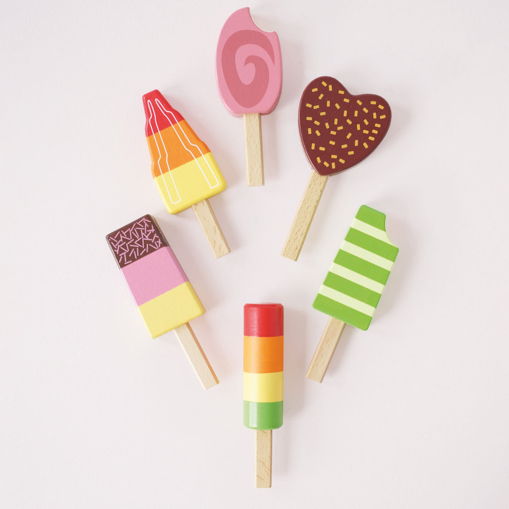 Six colorful wooden toy ice creams on sticks are arranged on a striped stand. They vary in shapes and vibrant designs, exuding a playful and whimsical tone.
