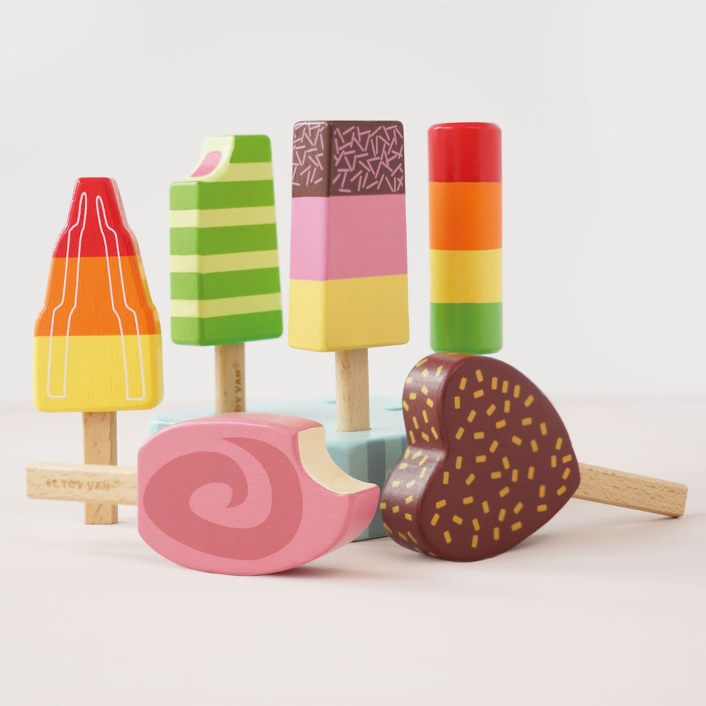 Six colorful wooden toy ice creams on sticks are arranged on a striped stand. They vary in shapes and vibrant designs, exuding a playful and whimsical tone.