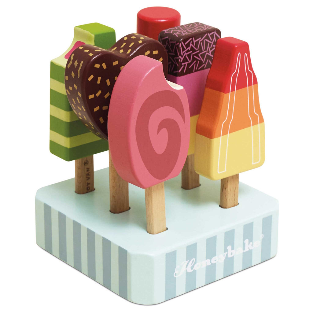 Six colorful wooden toy ice creams on sticks are arranged on a striped stand. They vary in shapes and vibrant designs, exuding a playful and whimsical tone.