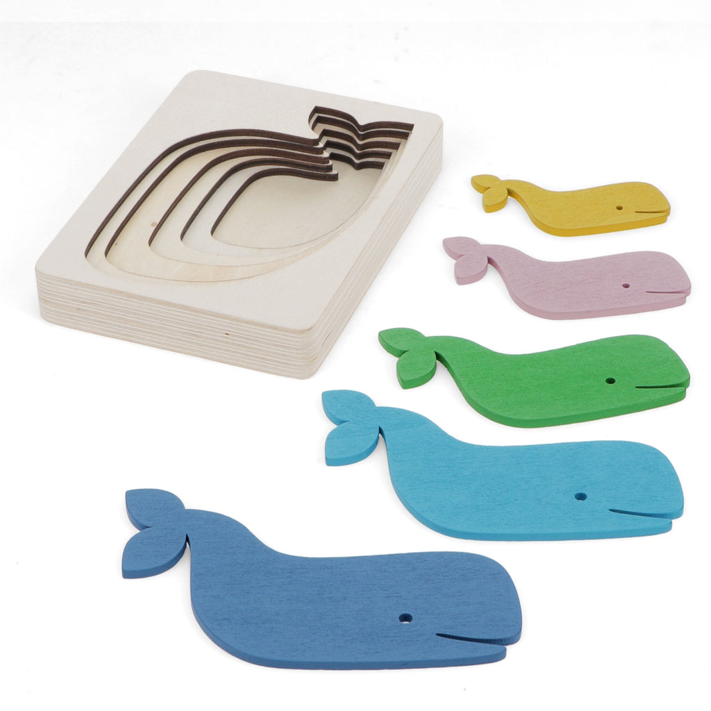 A colorful wooden whale puzzle featuring various whale shapes in pink, yellow, green, blue, and dark blue, alongside a layered wooden base.
