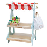 Wooden market stall toy with a red-striped awning, wooden fruit crate, bell, and shopping bag.