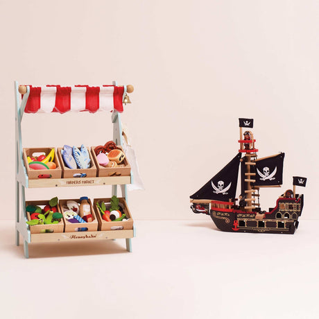 Wooden toy play set featuring a market stall with food crates next to a pirate ship.