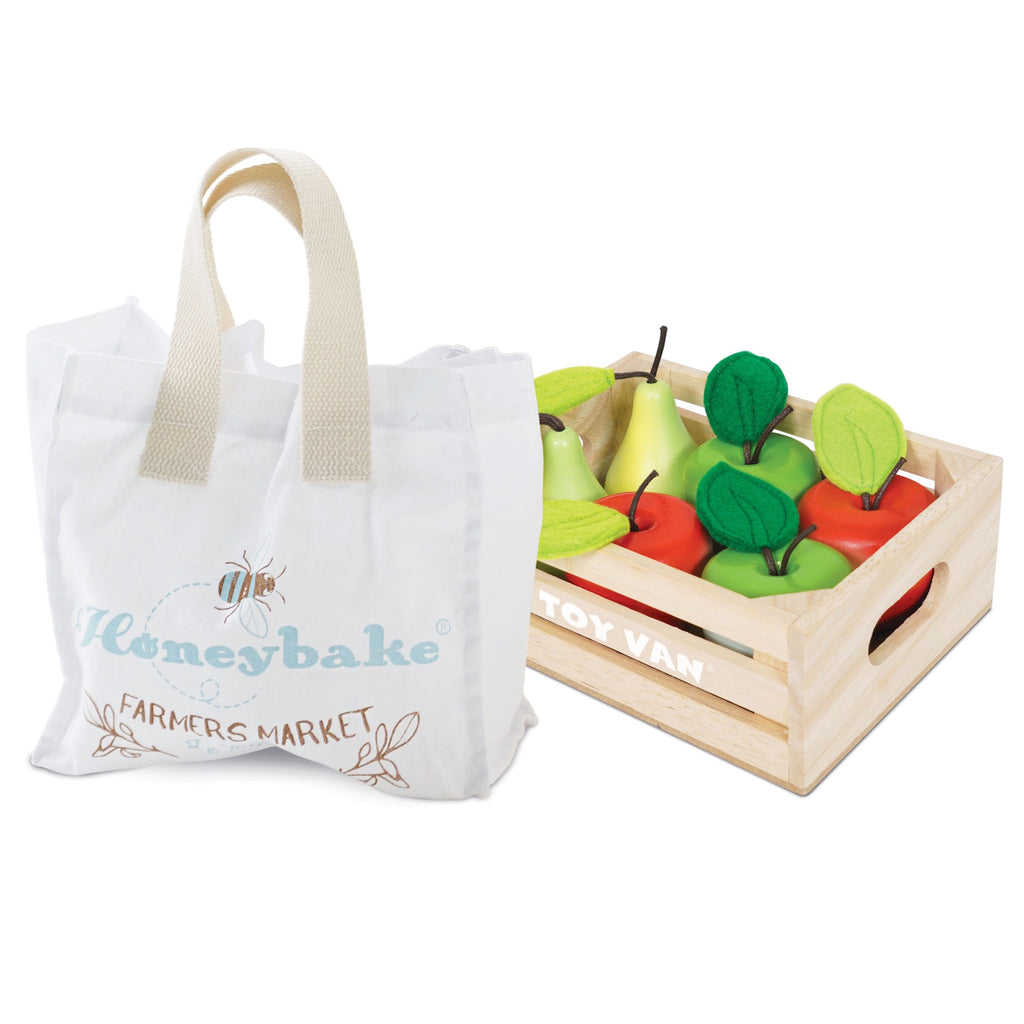 Toy crate with colorful wooden apples and pears beside a white fabric tote bag labeled "Farmers Market." Playful and vibrant setup.