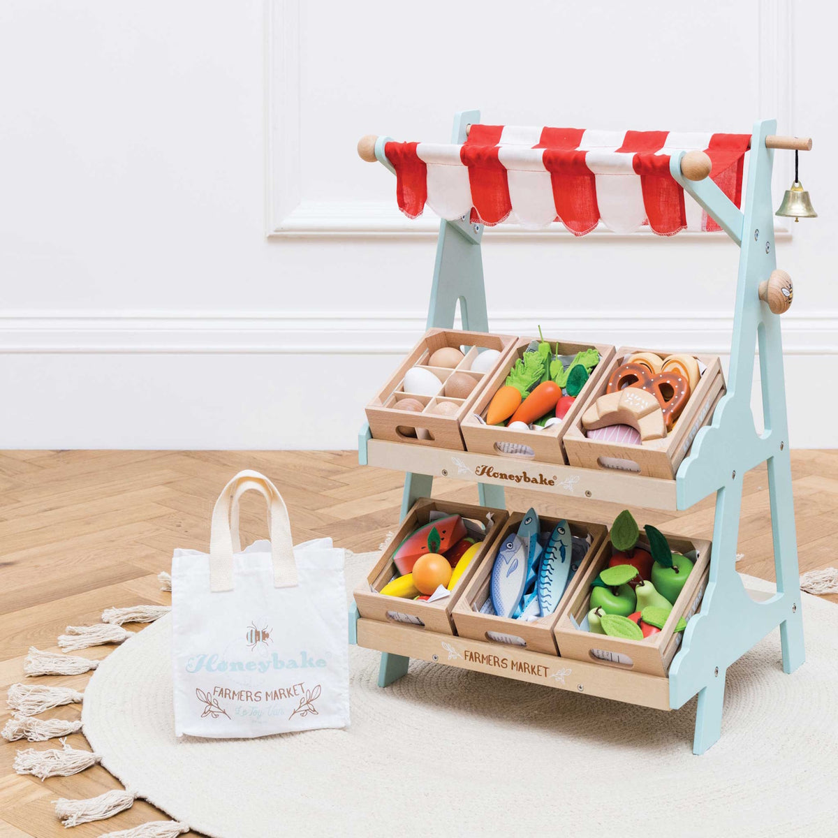 Wooden toy market stand with crates of play food, a striped canopy, and a canvas shopping bag.