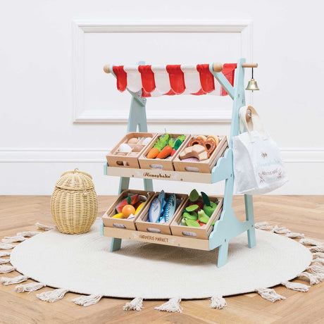 Wooden toy market stall with a red awning, filled with crates of play food and accessories.