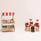 Wooden toy farmers market stall filled with play food crates next to a wooden toy castle.