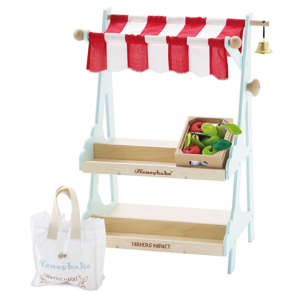 Toy market stall with red and white striped canopy and a bell. Features wooden tiers, a crate with toy fruits, and a canvas shopping bag labeled "Farmers Market."