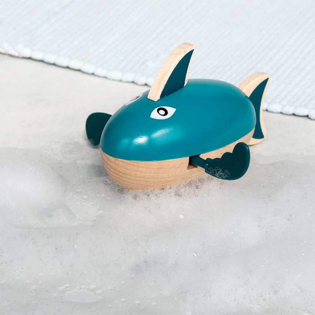 A playful wooden bath toy shaped like a shark that paddles through water when wound up.