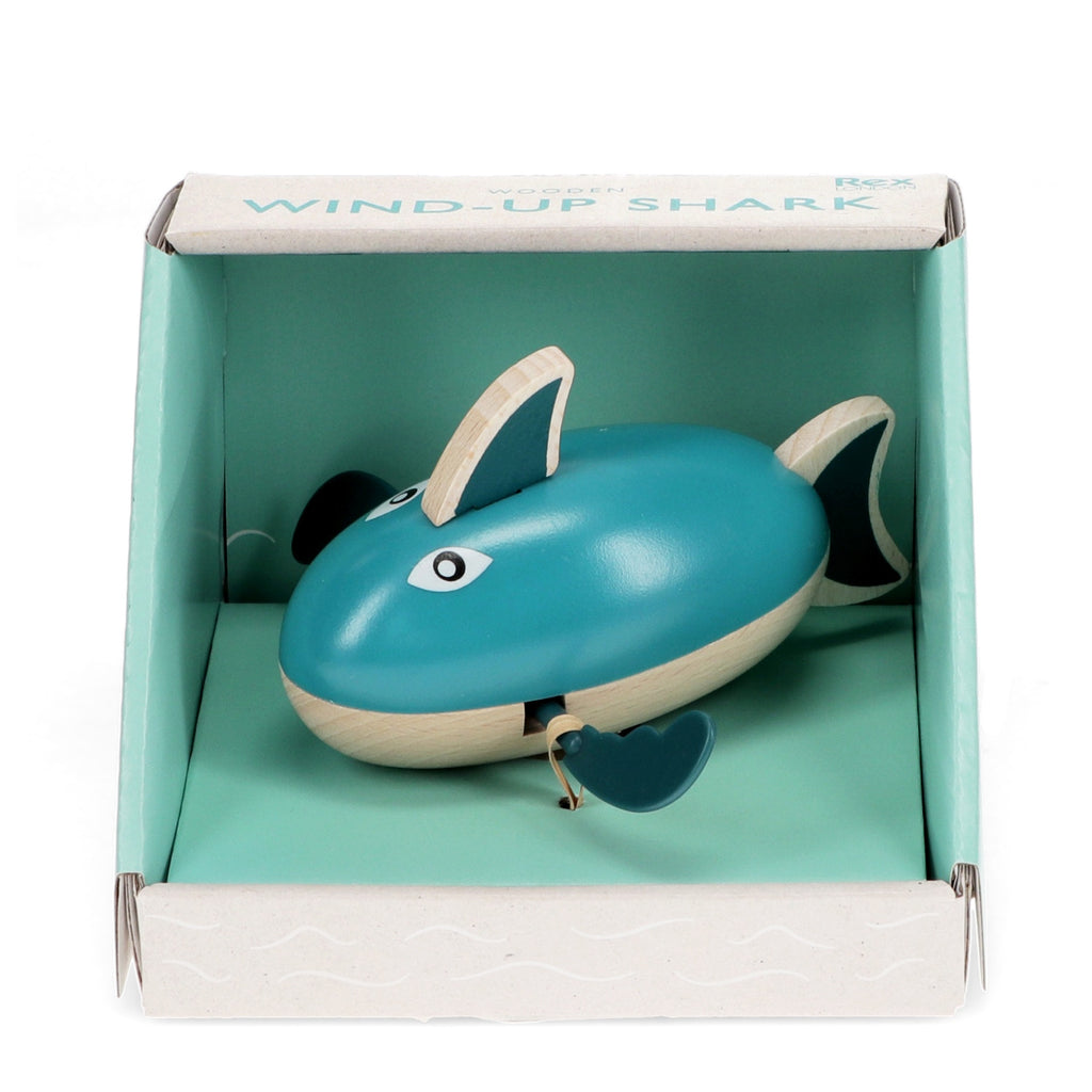 A playful wooden bath toy shaped like a shark that paddles through water when wound up.