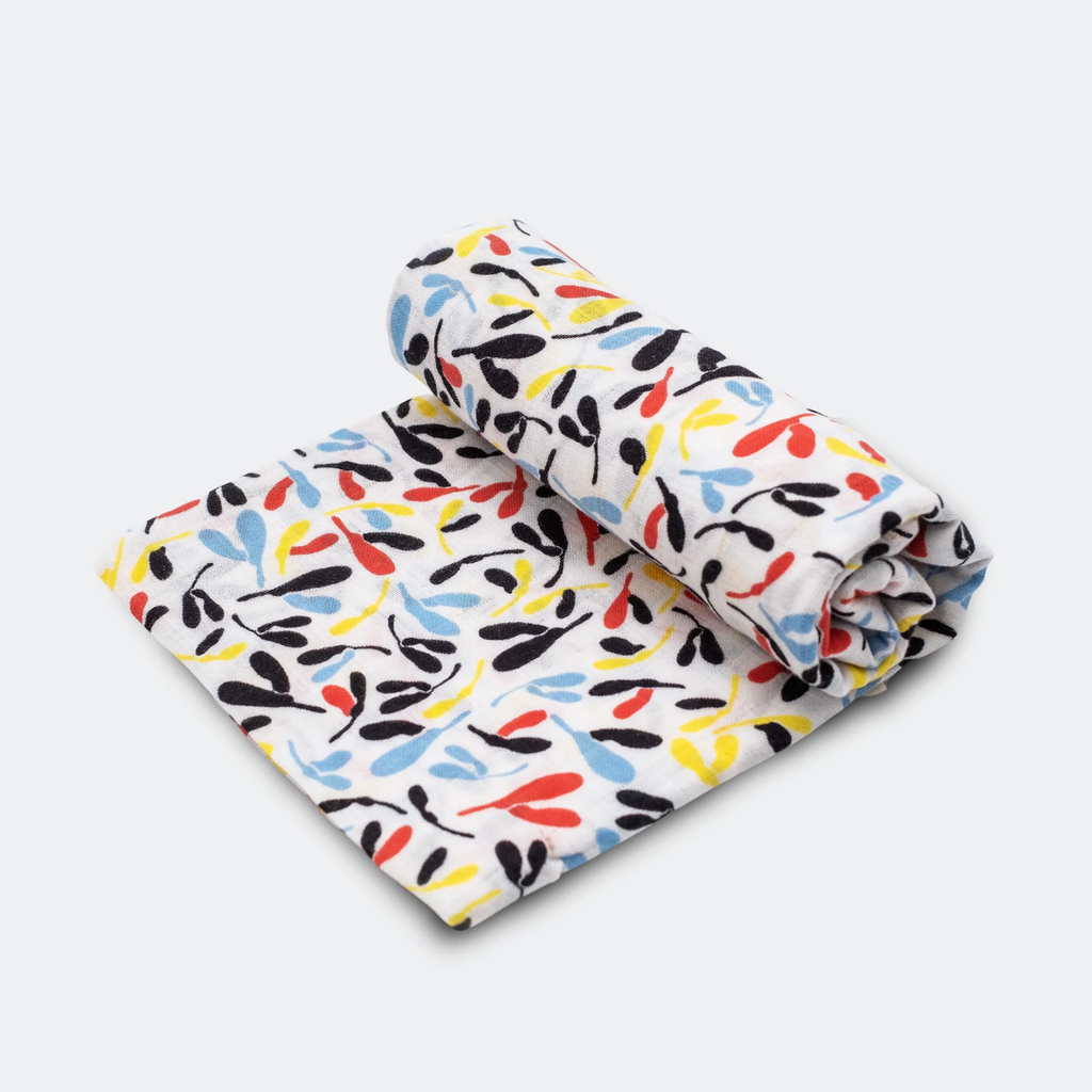 Rolled and folded white cloth with abstract leaf patterns in black, red, yellow, and blue, set against a light gray background. Conveys a playful tone.